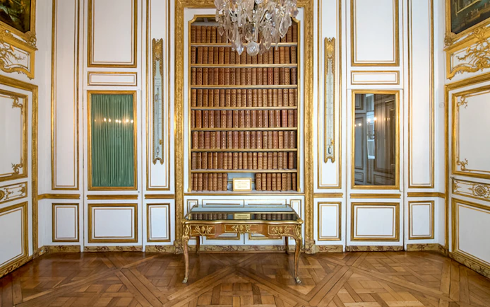 Bookshelf and ornate table in the Palace of Versailles library room.
