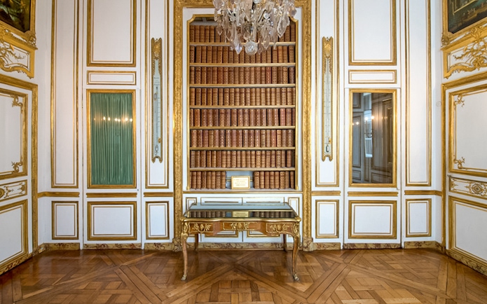 Bookshelf and ornate table in the Palace of Versailles library room.