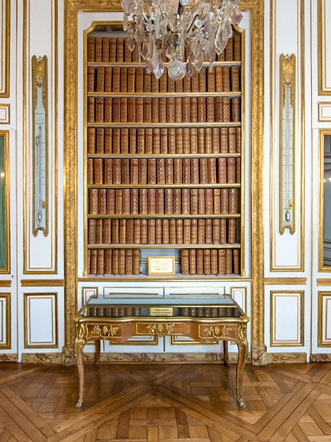 Bookshelf and ornate table in the Palace of Versailles library room.