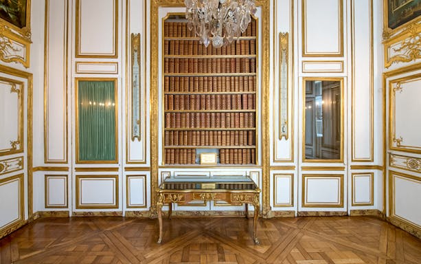 Bookshelf and ornate table in the Palace of Versailles library room.