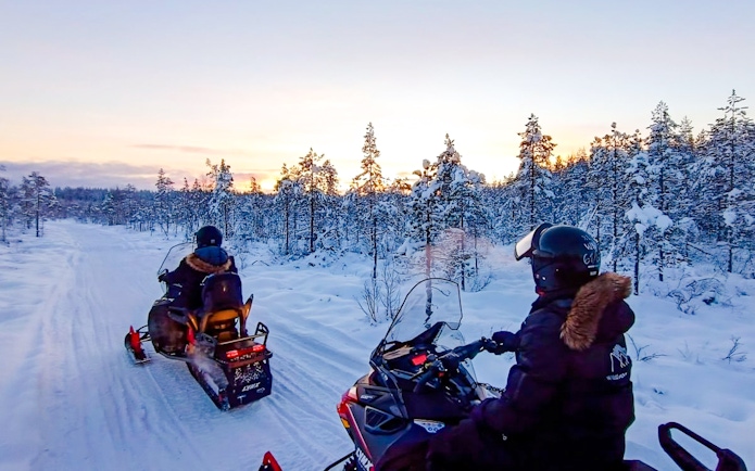 Snowmobilers riding through snowy forest during Rovaniemi safari adventure.