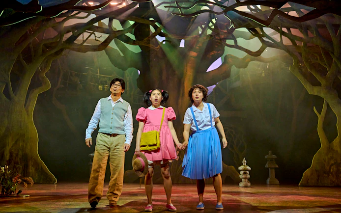 Stage scene from My Neighbour Totoro with three actors in a forest setting.