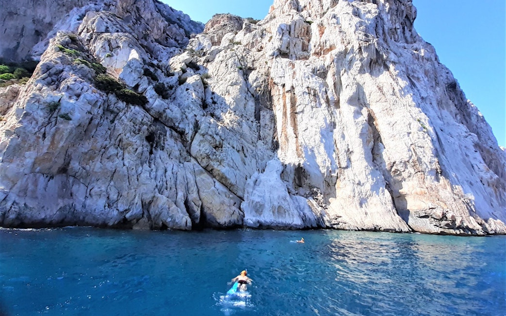 Snorkeler near rocky cliffs at Capo Figari, Sardinia, during dolphin sighting tour.