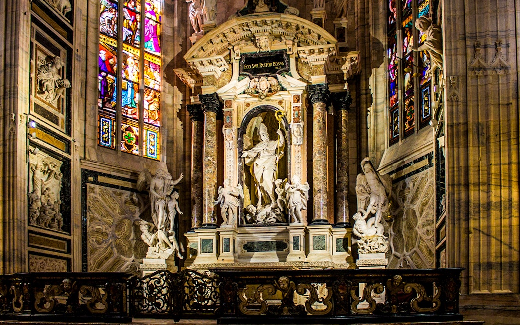 Interior of Milan Cathedral featuring ornate sculptures and stained glass windows, Italy.