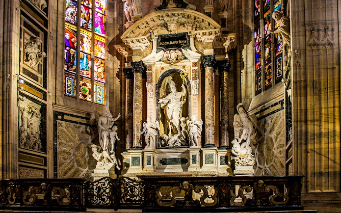 Interior of Milan Cathedral featuring ornate sculptures and stained glass windows, Italy.