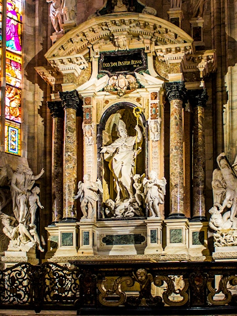 Interior of Milan Cathedral featuring ornate sculptures and stained glass windows, Italy.