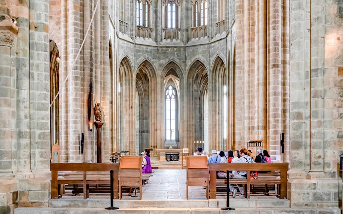 Visitors seated inside Mont-Saint-Michel Abbey, France, admiring Gothic architecture.