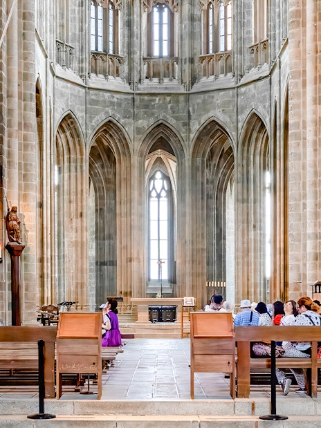 Visitors seated inside Mont-Saint-Michel Abbey, France, admiring Gothic architecture.