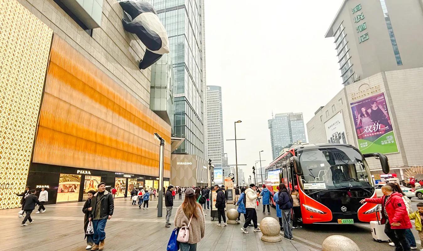 People walking near a shopping mall with a giant panda sculpture in Chengdu, China.