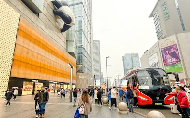 People walking near a shopping mall with a giant panda sculpture in Chengdu, China.