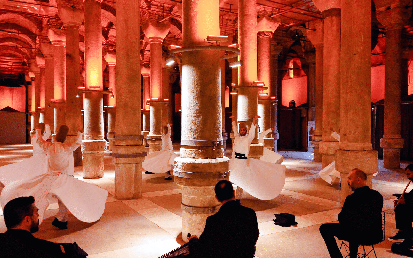 Whirling Dervishes performing in a historic Istanbul venue with musicians playing.