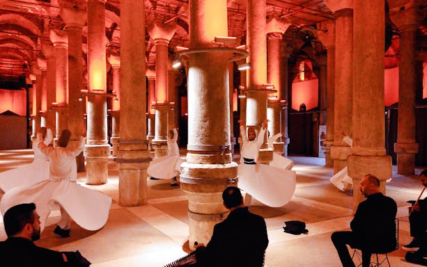 Whirling Dervishes performing in a historic Istanbul venue with musicians playing.