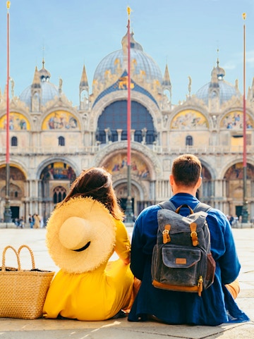 Couple sitting in St. Mark's Square, Venice, with Basilica di San Marco in the background.