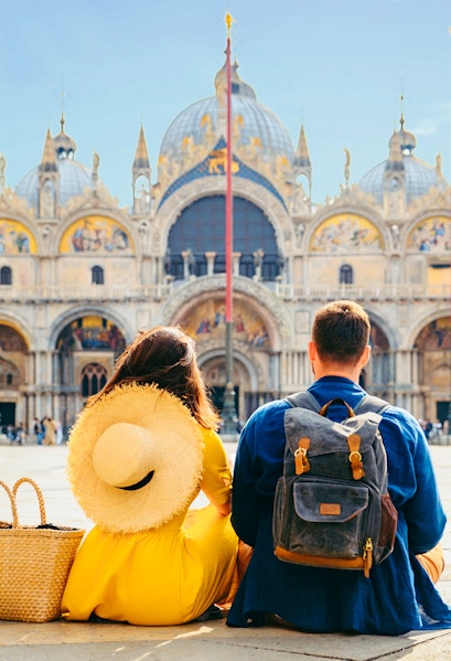 Couple sitting in St. Mark's Square, Venice, with Basilica di San Marco in the background.