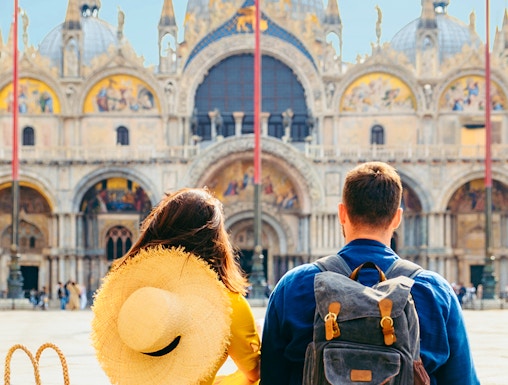 Couple sitting in St. Mark's Square, Venice, with Basilica di San Marco in the background.