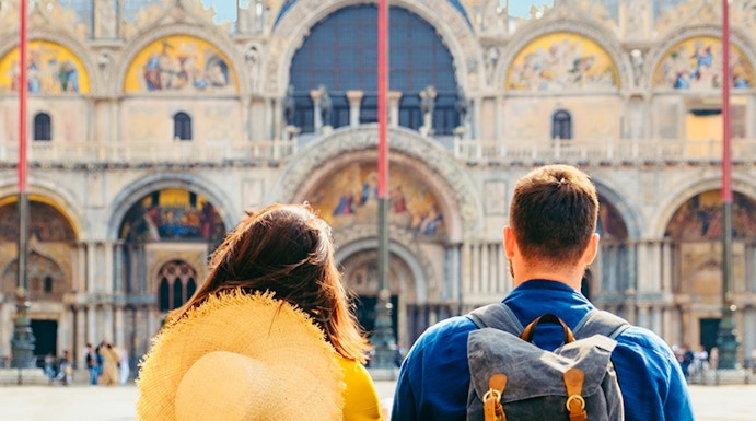 Couple sitting in St. Mark's Square, Venice, with Basilica di San Marco in the background.