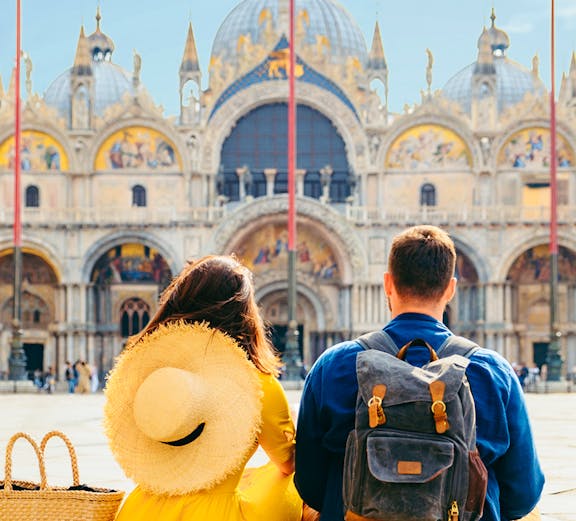Couple sitting in St. Mark's Square, Venice, with Basilica di San Marco in the background.