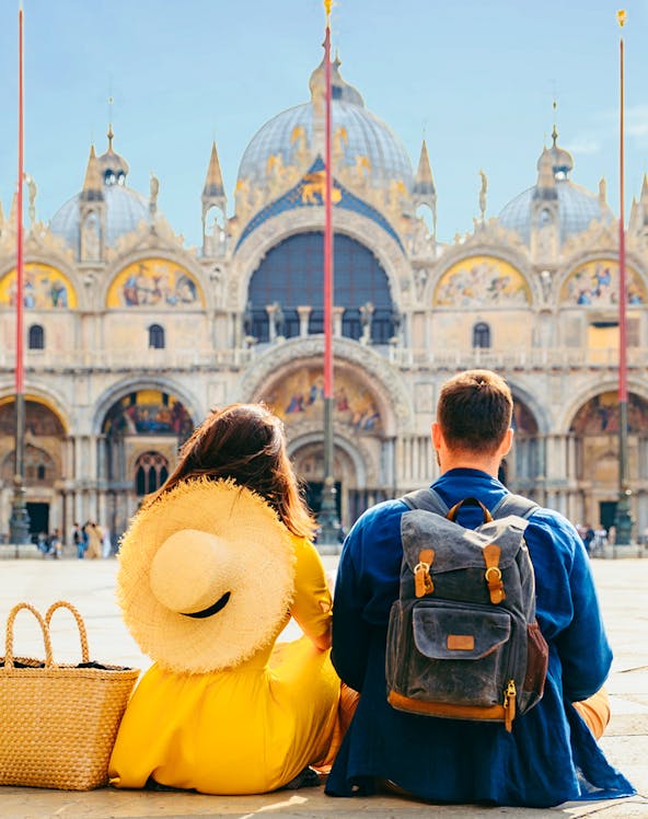 Couple sitting in St. Mark's Square, Venice, with Basilica di San Marco in the background.