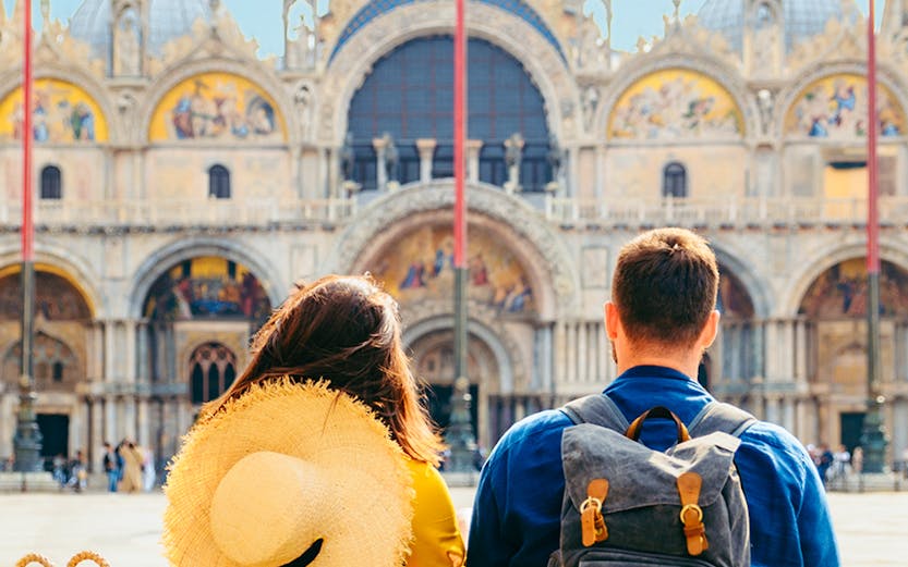 Couple sitting in St. Mark's Square, Venice, with Basilica di San Marco in the background.
