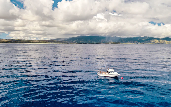 Boat on ocean with tourists during O'ahu Shark Dive Tour, Hawaii, with mountains in the background.