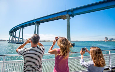 Guests on a San Diego cruise looking for whales and dolphins near a bridge.