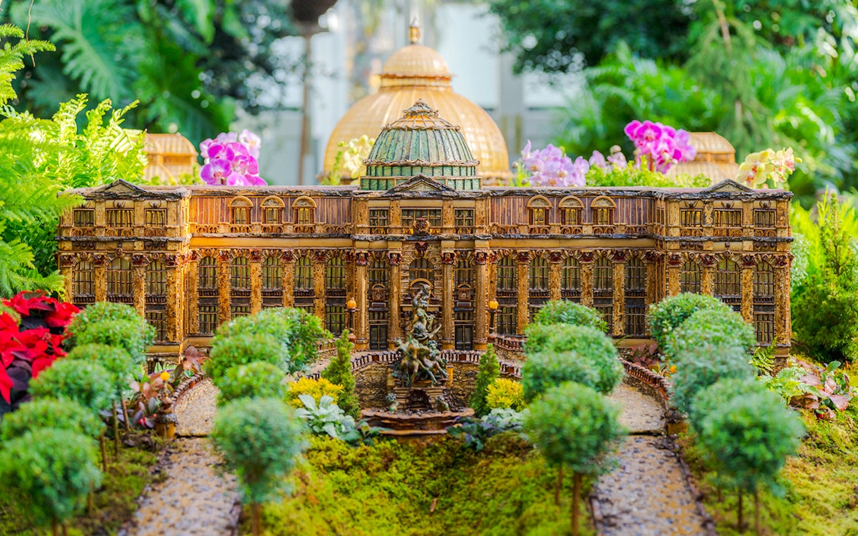 Miniature building display at NYBG Holiday Train Show, surrounded by lush greenery and flowers.