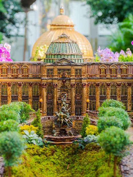 Miniature building display at NYBG Holiday Train Show, surrounded by lush greenery and flowers.