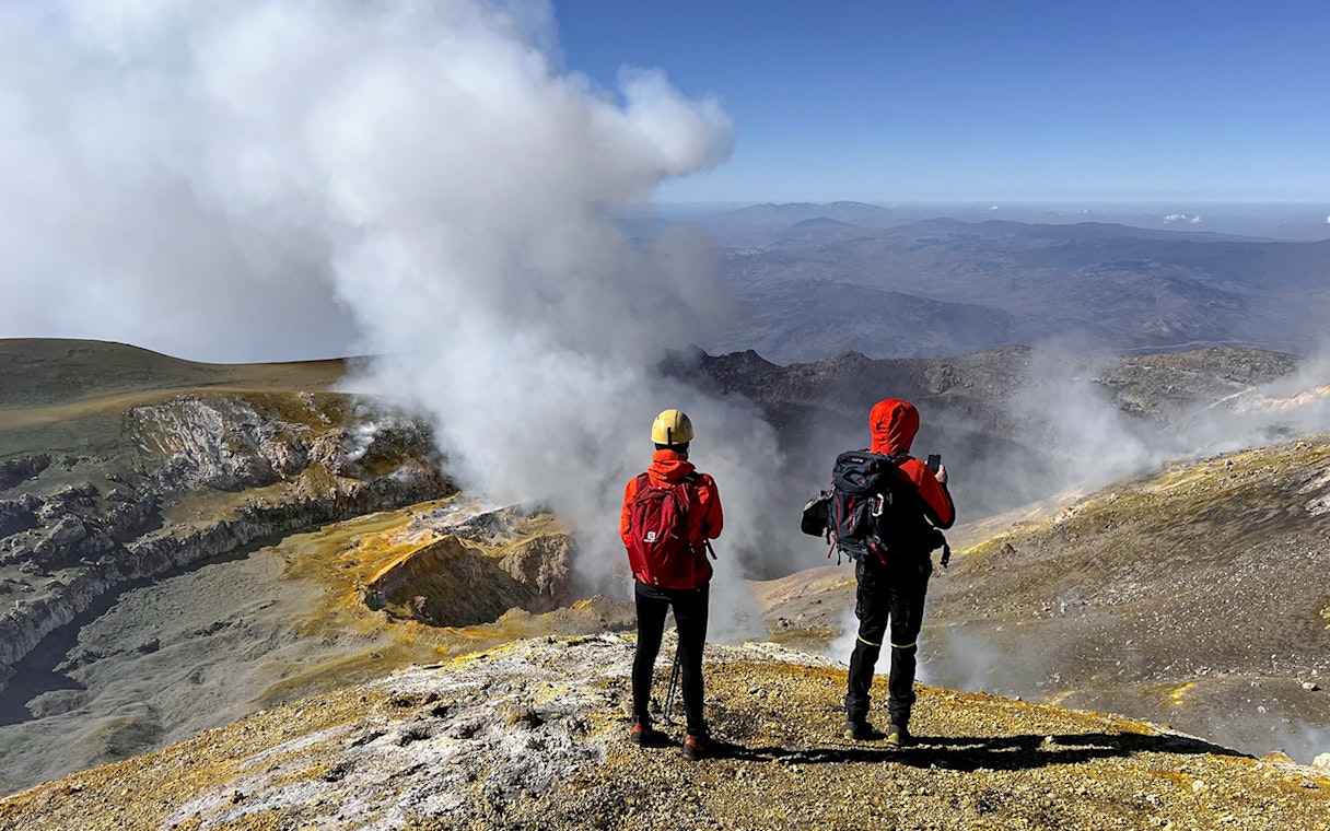 Couple standing at Mount Etna summit, viewing volcanic landscape and steam vents.
