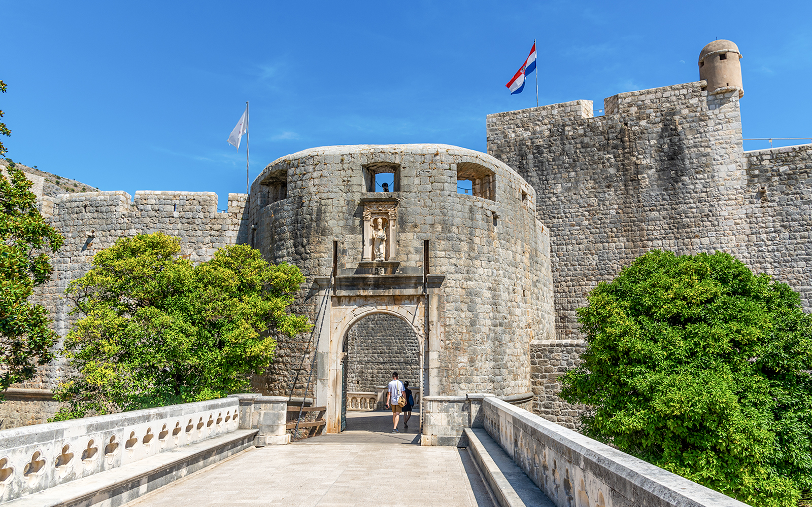 Pile Gate entrance to Dubrovnik's Old Town with stone walls and Croatian flag.