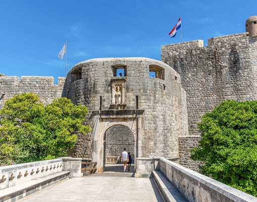 Pile Gate entrance to Dubrovnik's Old Town with stone walls and Croatian flag.