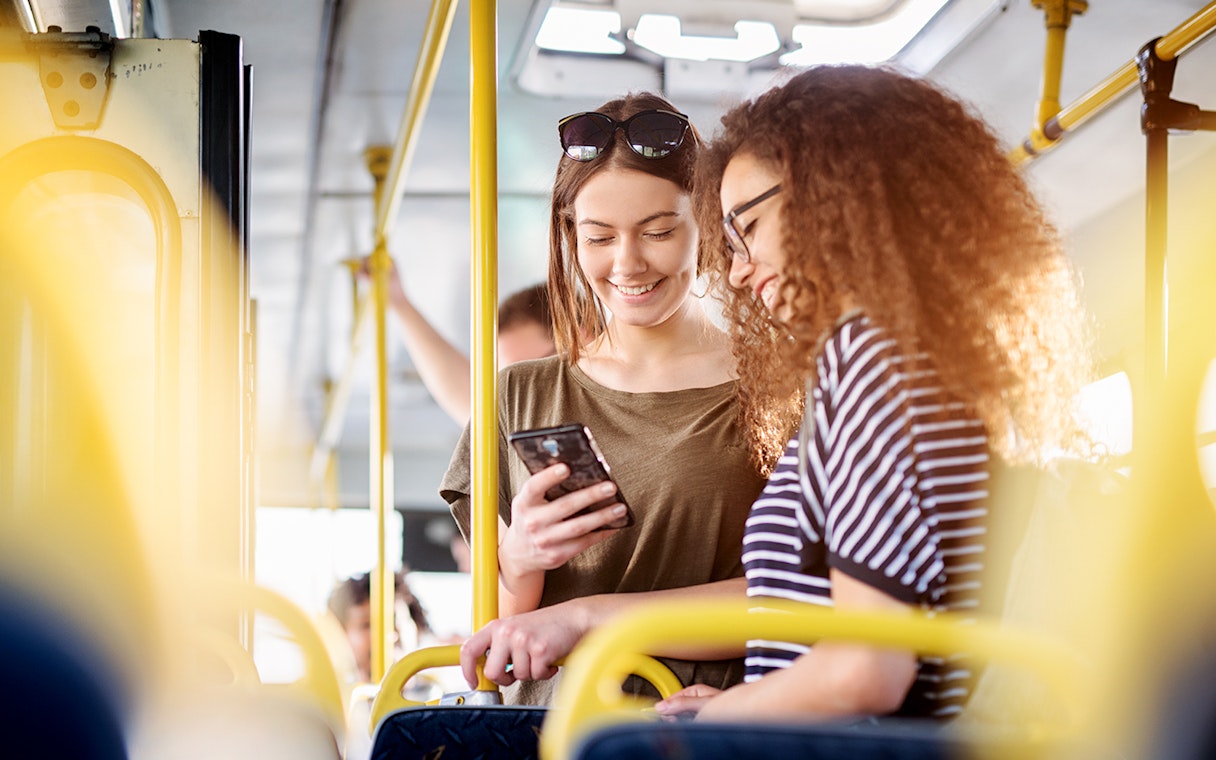 Two women on a bus checking phone, Fiumicino Airport to Naples transfer.