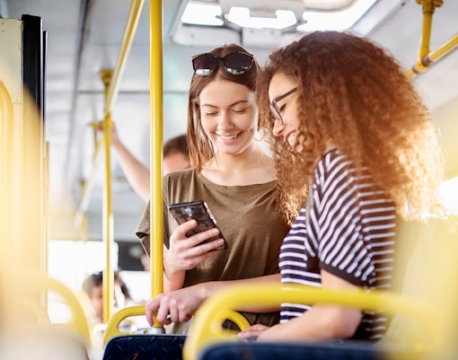 Two women on a bus checking phone, Fiumicino Airport to Naples transfer.