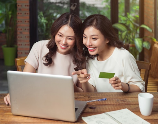 Two women booking city card for Vienna online with a laptop and credit card.