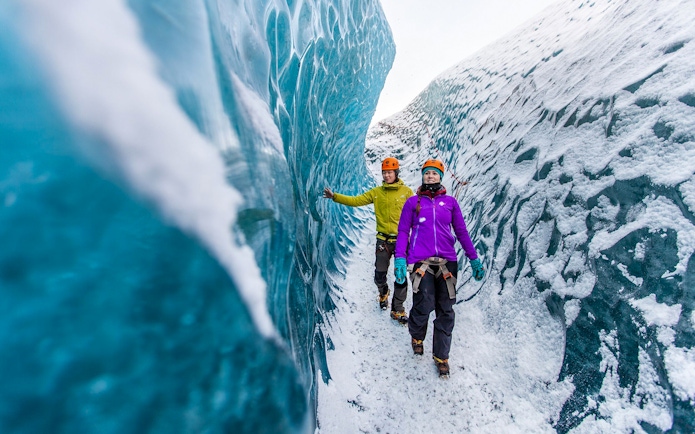 Hikers exploring icy crevasse on Falljökull glacier.