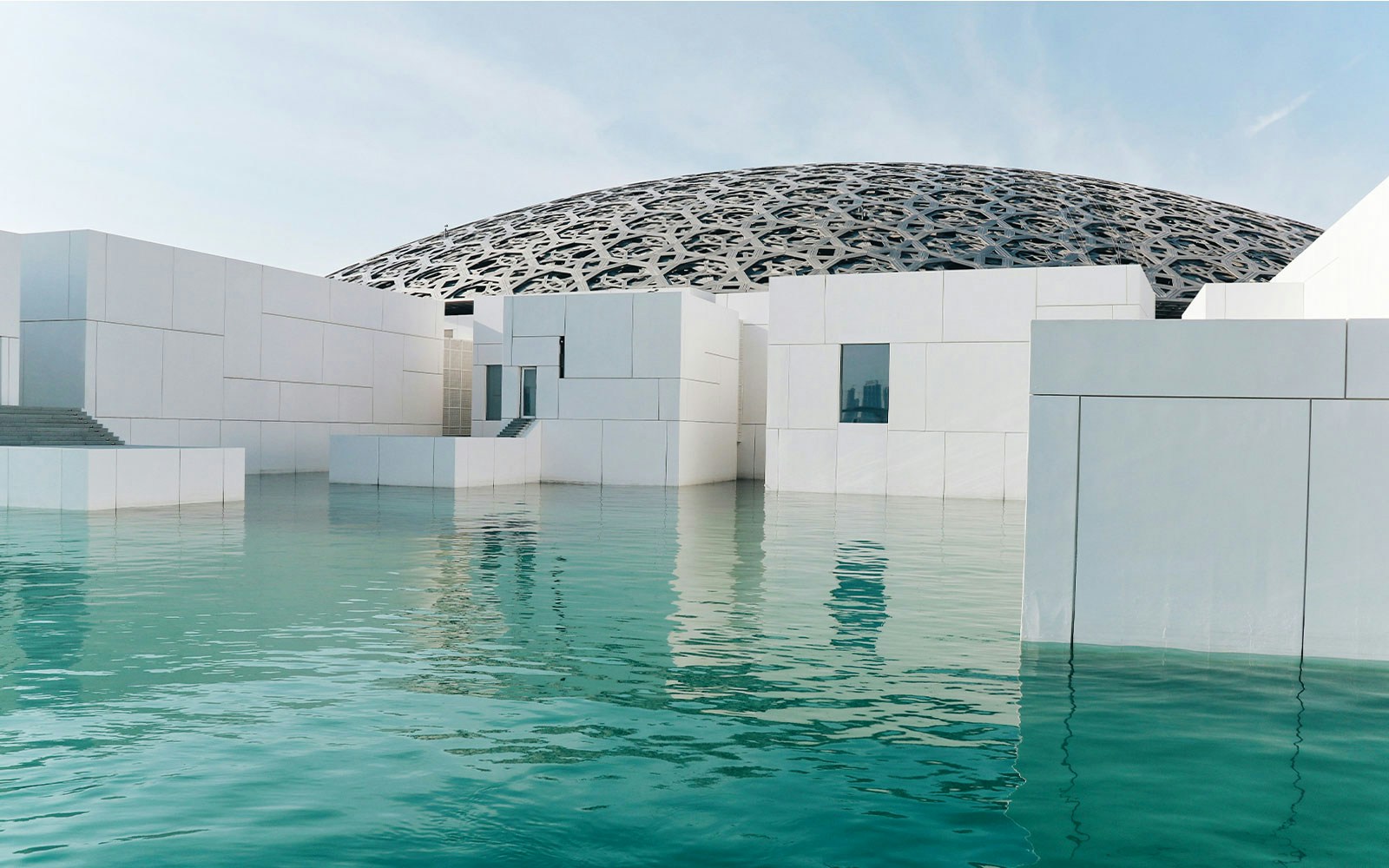 Louvre Museum Abu Dhabi exterior with dome and reflecting water.
