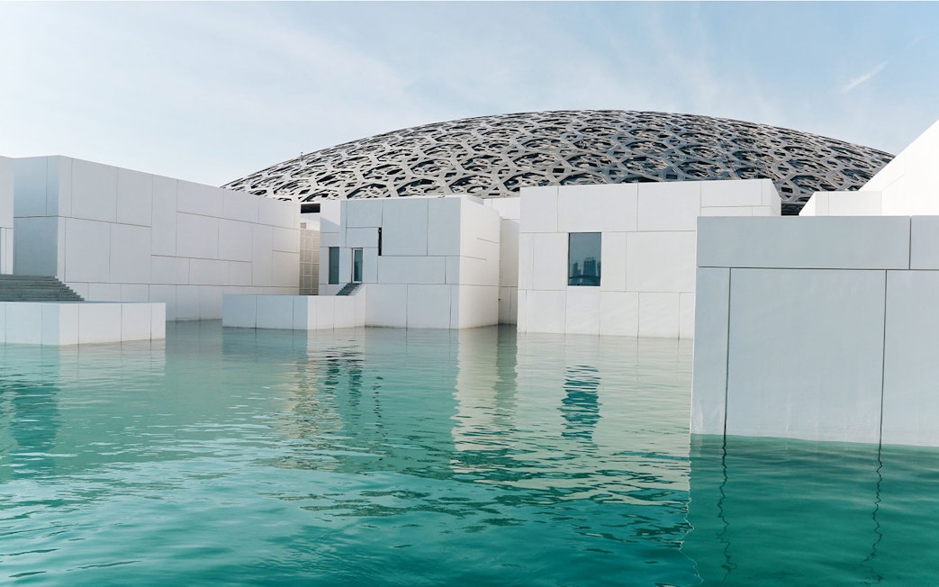 Louvre Museum Abu Dhabi exterior with dome and reflecting water.