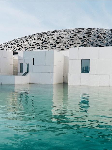 Louvre Museum Abu Dhabi exterior with dome and reflecting water.
