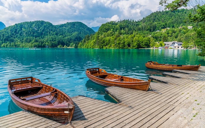 Boats moored along the shore of Lake Bled with forested hills in the background.