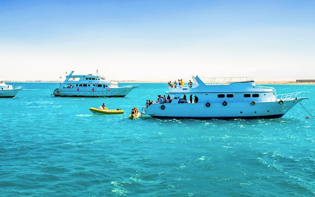 Snorkeling tour boats in Orange Bay, Egypt, with tourists on deck and a small yellow boat nearby.
