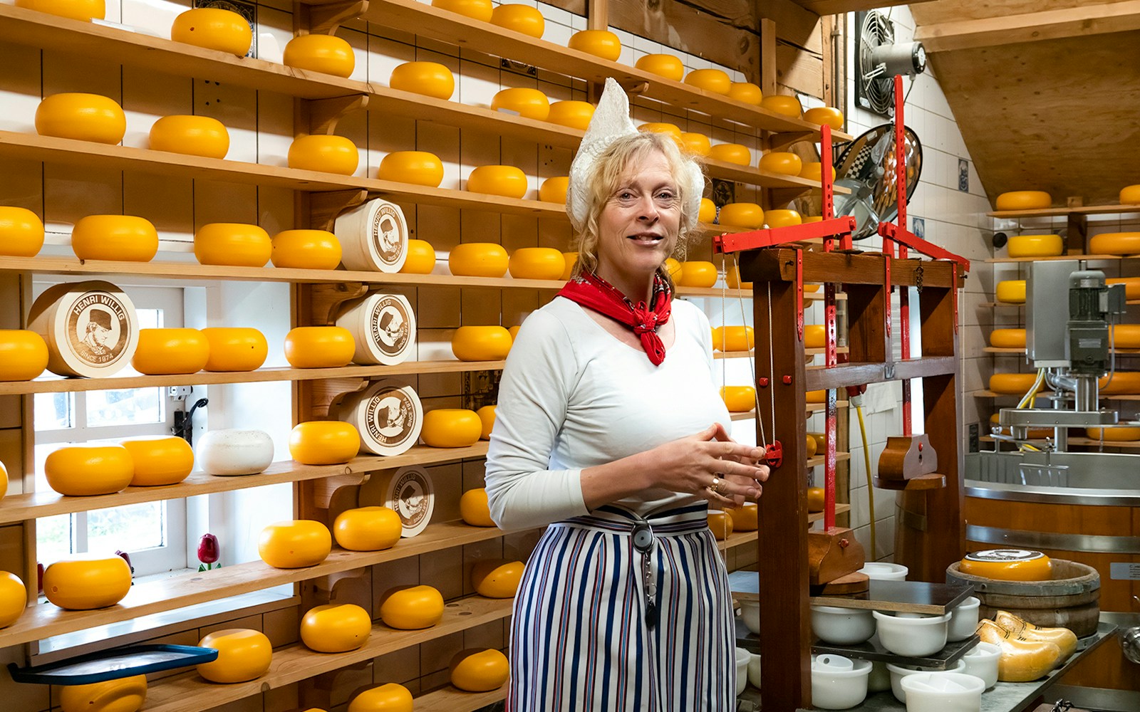 Cheese maker at Zaanse Schans cheese farm with shelves of cheese wheels.