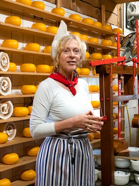 Cheese maker at Zaanse Schans cheese farm with shelves of cheese wheels.