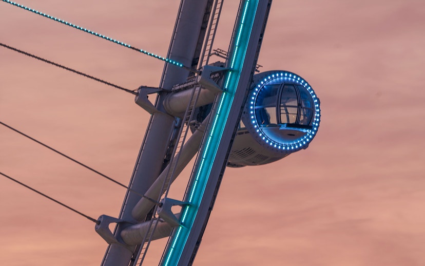 Ain Dubai pod illuminated at sunset against a pink sky.