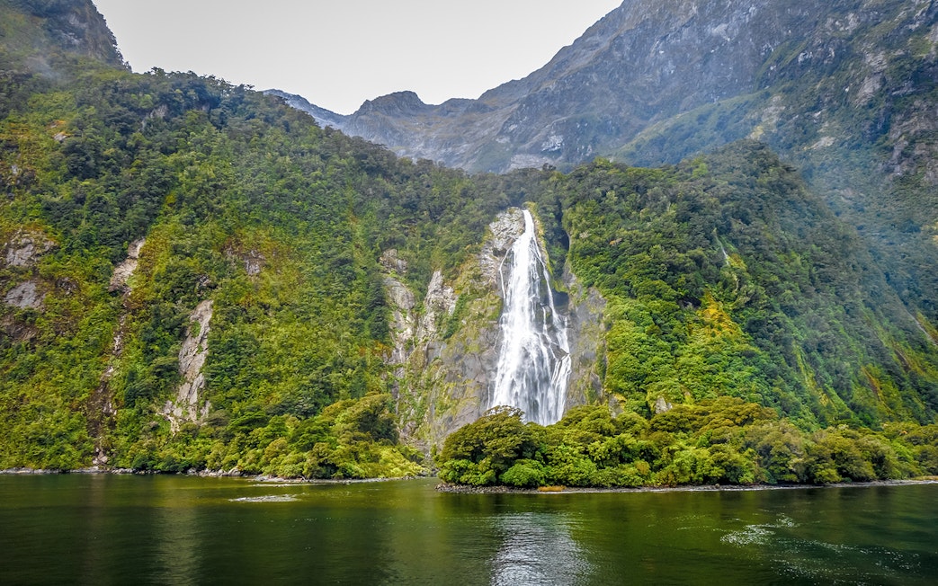Waterfall cascading down lush green mountains in Milford Sound, Queenstown day trip.