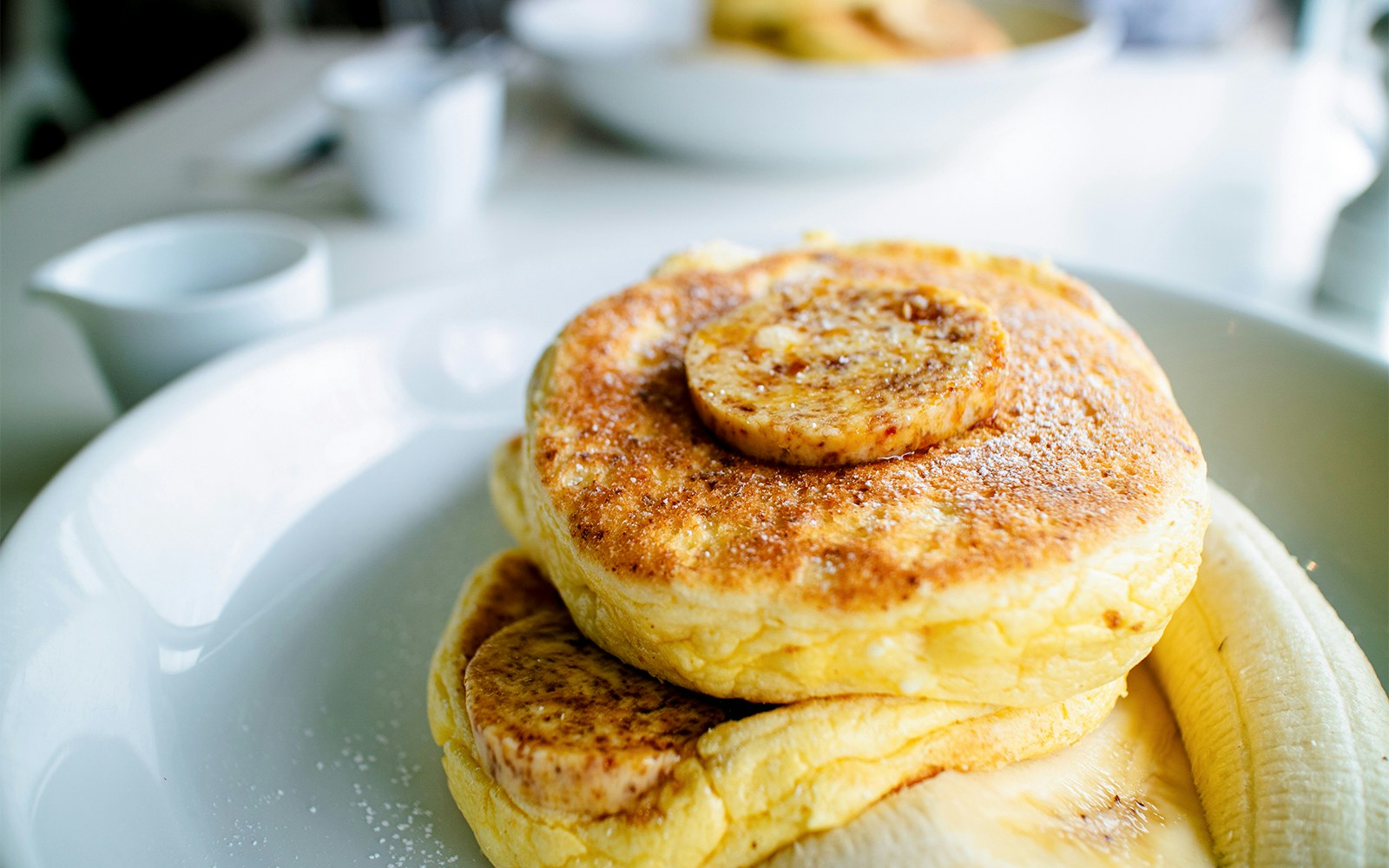 Banana ricotta pancakes topped with fresh bananas and syrup on a white plate.