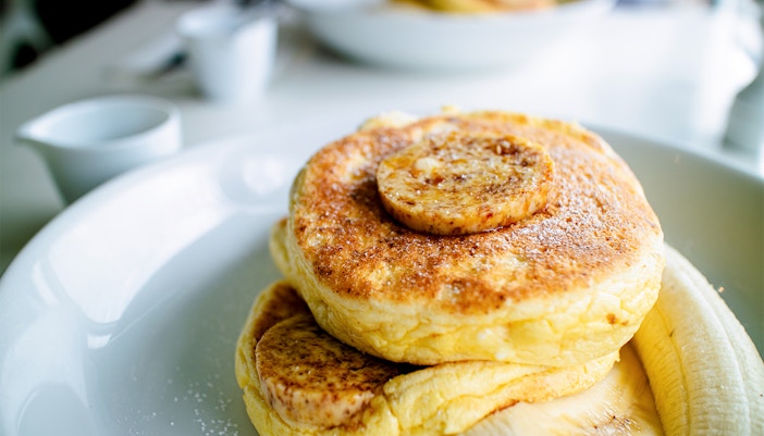 Banana ricotta pancakes topped with fresh bananas and syrup on a white plate.