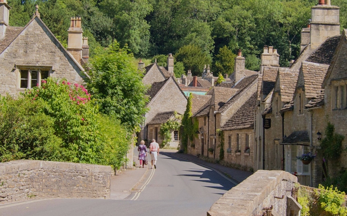 Stone cottages along a narrow street in a Cotswold village, surrounded by greenery.