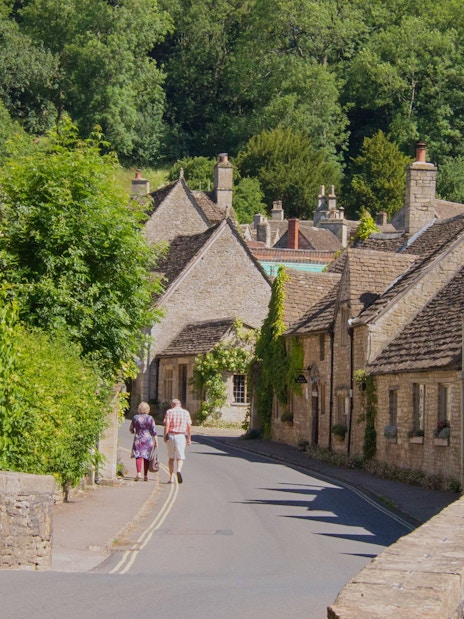Stone cottages along a narrow street in a Cotswold village, surrounded by greenery.