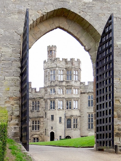 Warwick Castle gate open with view of historic stone building and manicured hedges.