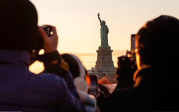 Guests photographing the Statue of Liberty at sunset, New York City.