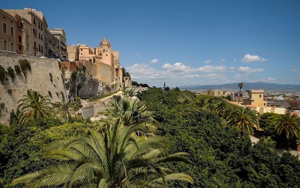 Cagliari's historic center with ancient buildings and lush greenery under a clear sky.